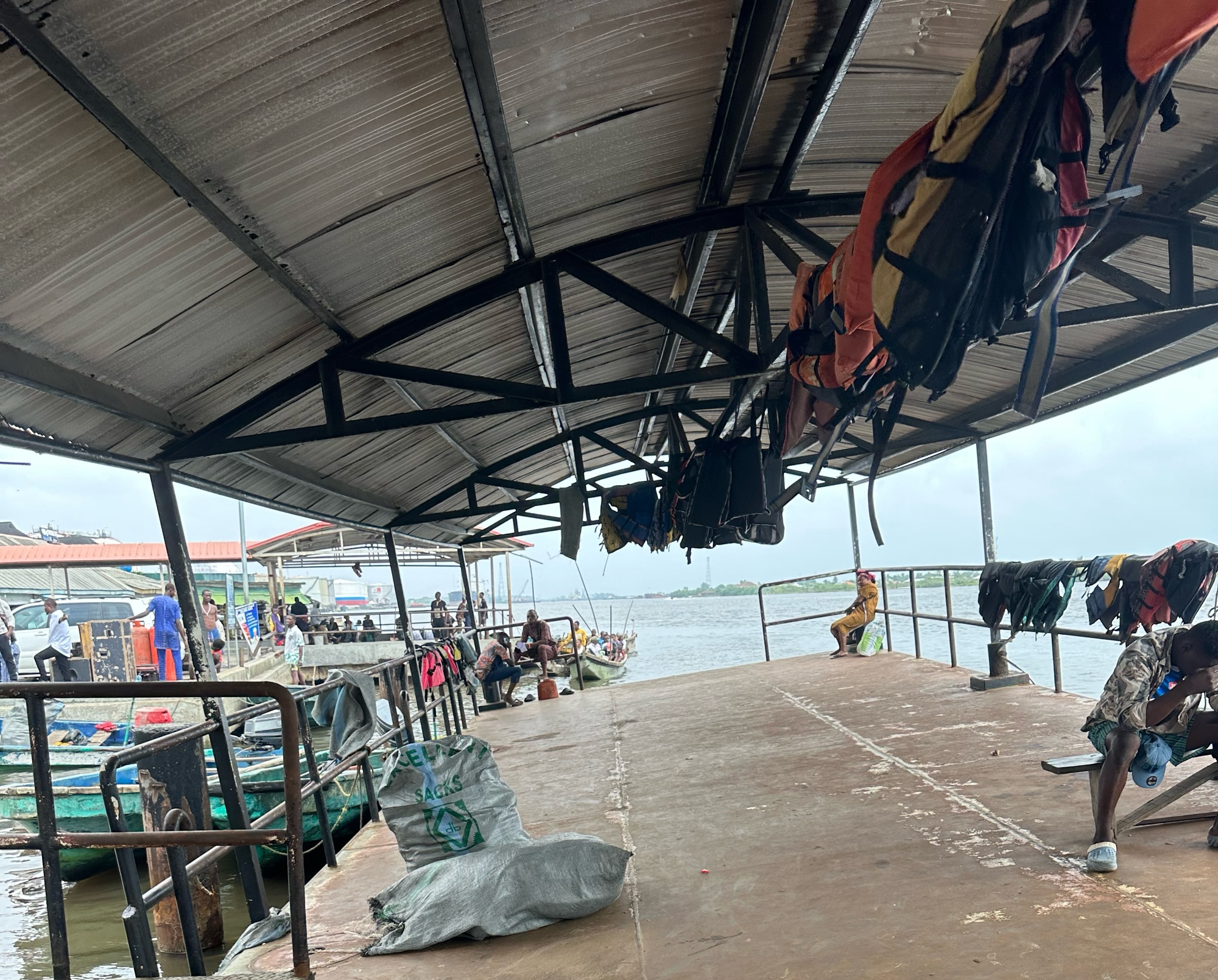 A walk way leading to a huge body of water. It has rails on both sides. By the left side there are boats in the water