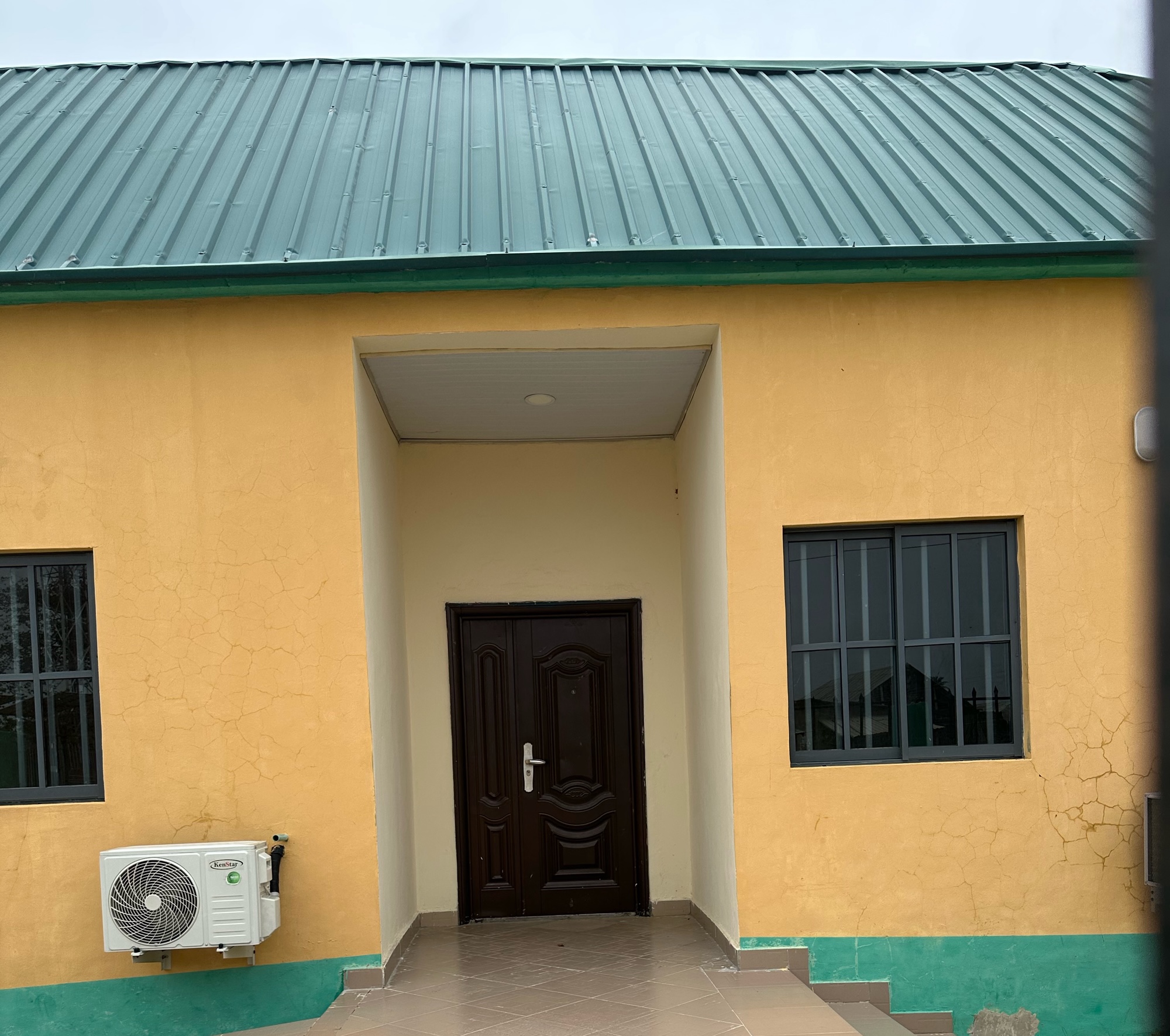 A building showing one window on the left and another on the right. In between is a door
