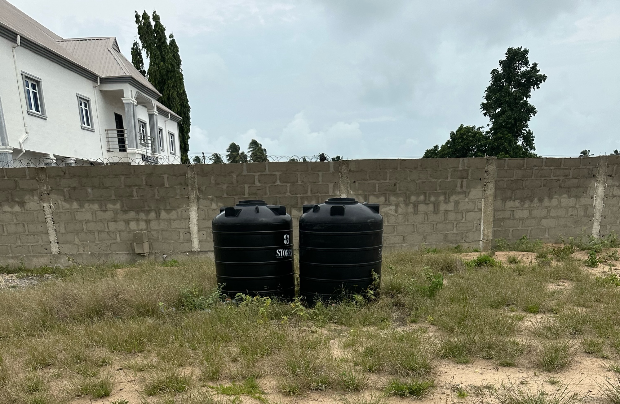 Two huge plastic tanks on a land. Behind the tanks is a fence