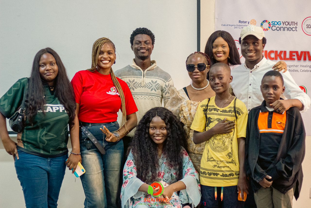 Eight people standing and a lady in a wheelchair indoors