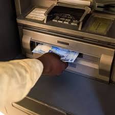 A hand holding a cash coming out of a cash outlet section of machine