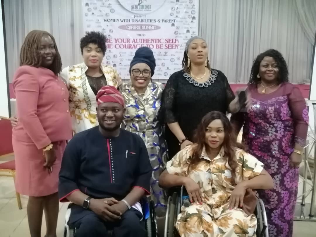 Image of Six women and one man indoor. One of the women is in front together with the man and both are on a wheelchair. The ma