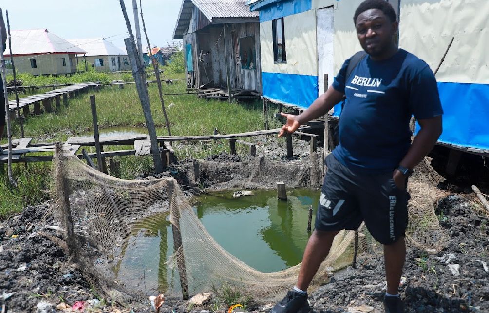 A man standing outdoors next to a small body of water with nets around the water
