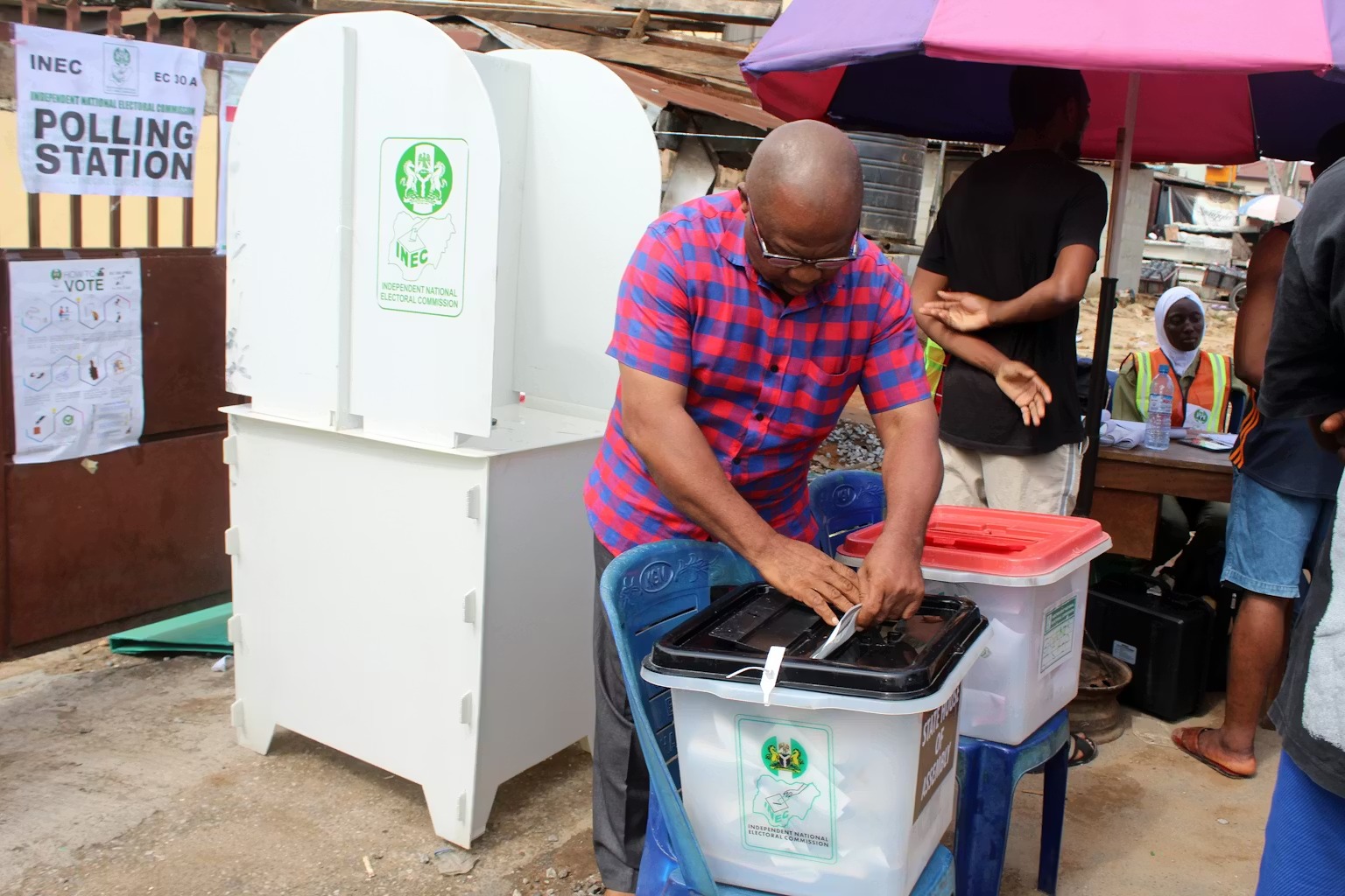 A man voting outdoors. He is putting a paper into a plastic box