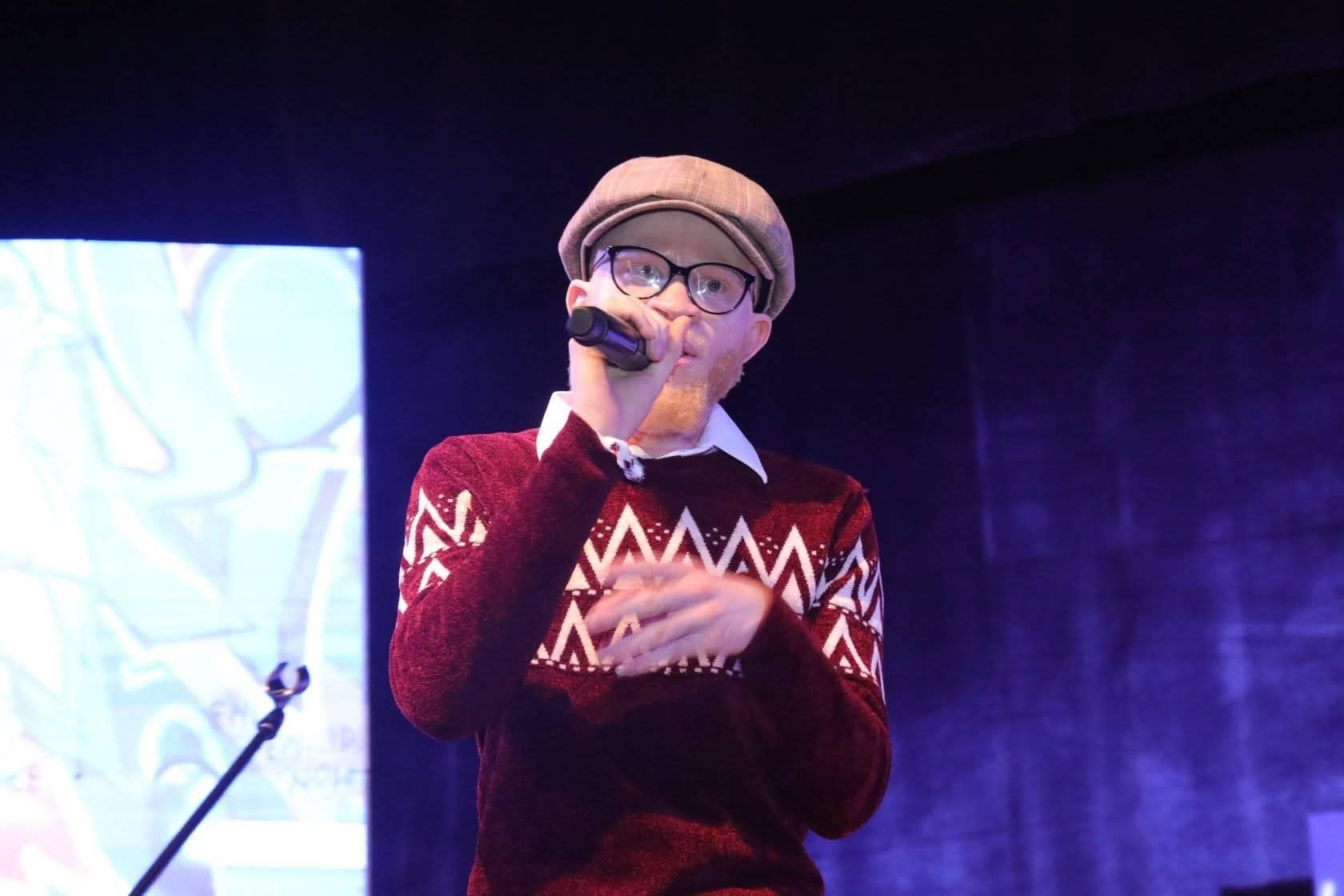 A man with albinism holding a microphone on stage.