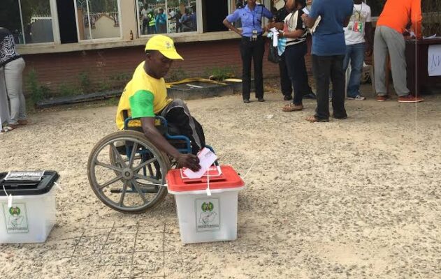 Image of a man in wheelchair casting a vote outdoors